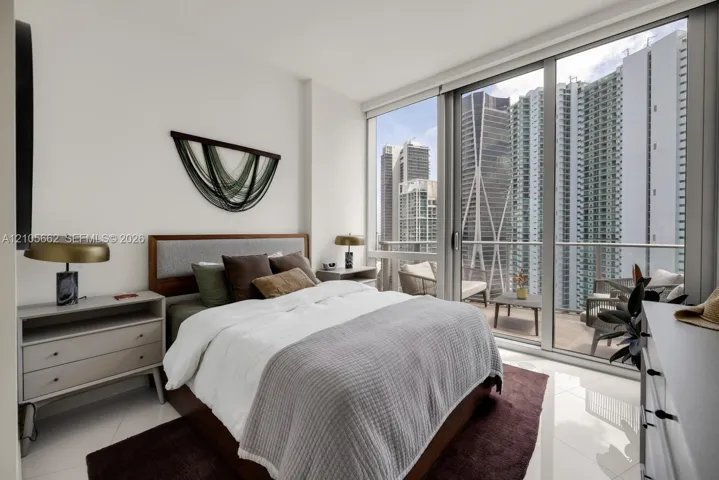 Floor-to-ceiling windows, polished light-toned tile flooring, and a private balcony featuring a glass-railing system