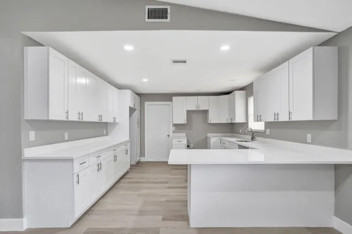Kitchen featuring white shaker-style cabinetry, solid-surface countertops, a breakfast bar peninsula, recessed lighting, and wood-finish flooring
