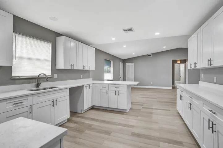 Kitchen featuring white shaker-style cabinetry, solid-surface countertops, wood-finish flooring, stainless steel undermount sink, and recessed lighting