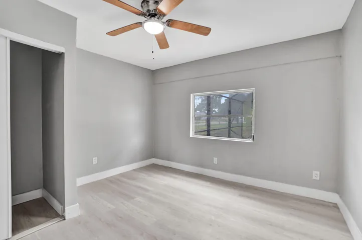 Neutral-toned interior space featuring light wood-finish flooring, a ceiling fan with integrated lighting, and a closet with sliding doors