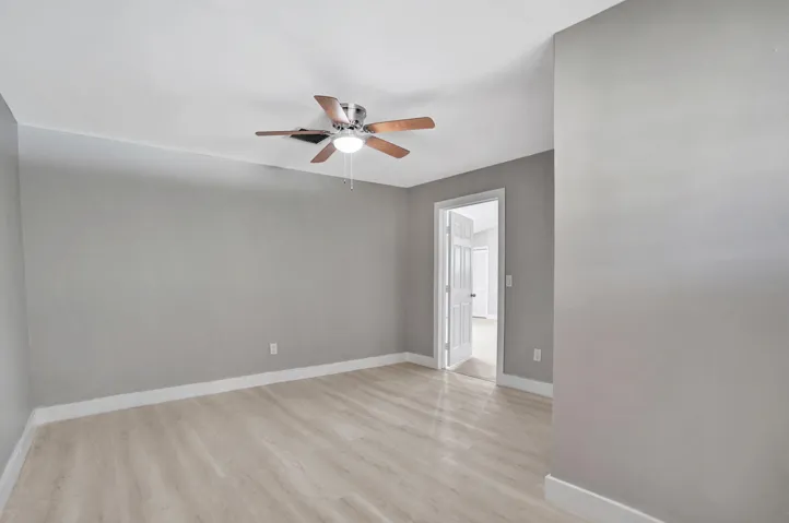 Neutral interior space featuring wood-finish flooring, light grey walls, and a ceiling-mounted light fixture with a five-blade fan