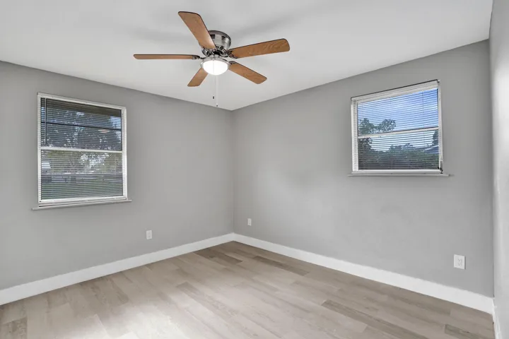 Neutral-toned interior featuring wood-finish flooring, dual windows with blinds, and a central ceiling fan with an integrated light fixture