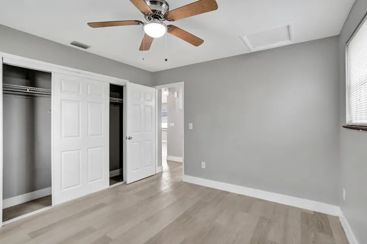 Neutral-toned interior featuring wood-finish flooring, a multi-blade ceiling fan with integrated lighting, and a closet with multi-panel doors
