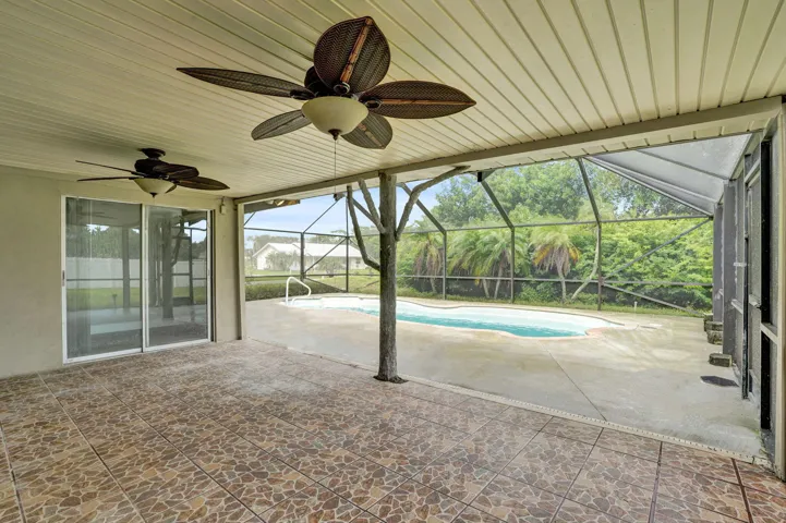Covered patio with patterned tile flooring, two ceiling fans, screen-enclosed pool area, and concrete decking