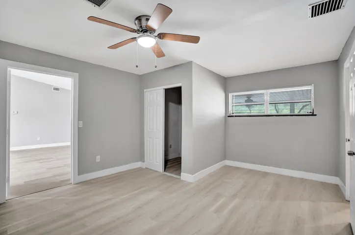 Room featuring wood-finish flooring, a multi-blade ceiling fan with integrated lighting, a horizontal sliding window, and a paneled closet door