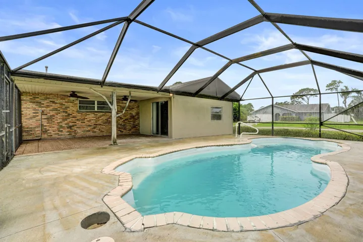 Screened-in pool enclosure with a concrete deck, multi-tone brick wall accent, and two ceiling fans