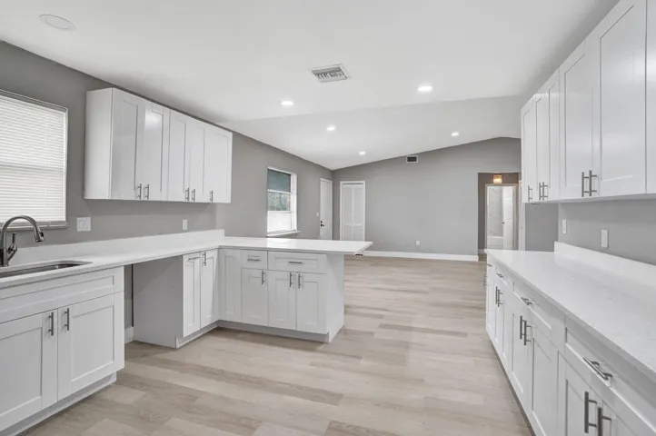 Kitchen featuring white shaker-style cabinetry, solid-surface countertops, wood-finish flooring, recessed lighting, and a vaulted ceiling