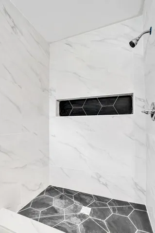 Walk-in shower featuring large-format white wall tile with grey veining, matte black hexagonal floor tile, a matching integrated horizontal recessed niche, and a polished chrome shower head