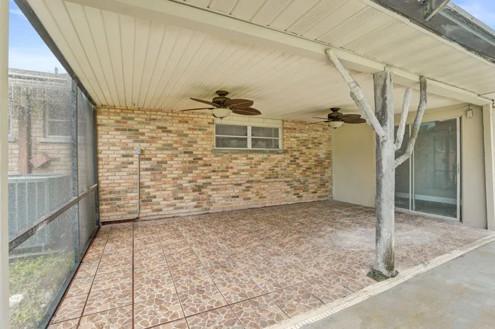 Screened-in patio featuring a textured tile floor, exposed brick exterior wall, dual ceiling fans, and a covered ceiling