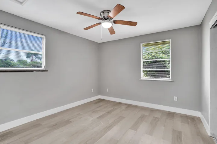 Neutral-toned interior featuring wood-finish flooring, dual windows with blinds, and a central ceiling fan with integrated lighting