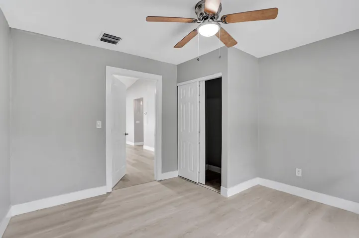 Neutral-toned walls, wood-finish flooring, ceiling fan with integrated light, and closet with sliding panel doors