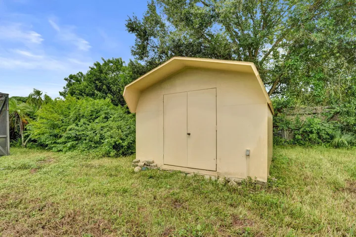 Detached storage structure featuring a gambrel roof, dual swinging entry doors, and an exterior electrical outlet