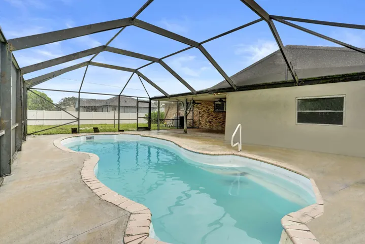 Screened-in patio featuring a freeform swimming pool, concrete deck, metal enclosure, and brick exterior accent