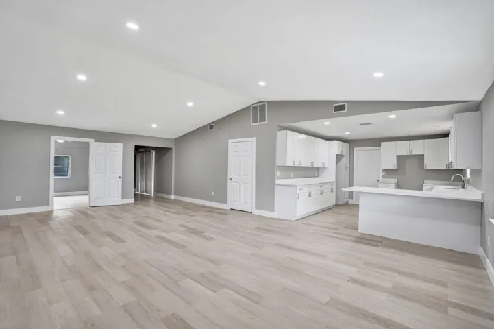 Open-concept interior featuring vaulted ceilings, wood-finish flooring, recessed lighting, white cabinetry, and a peninsula breakfast bar