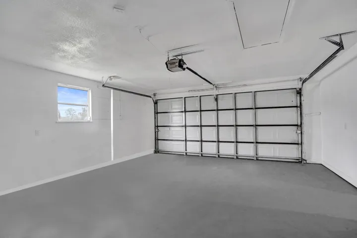 Two-car garage featuring a sectional metal door, concrete flooring, finished walls, an automated door opener, and a singular window