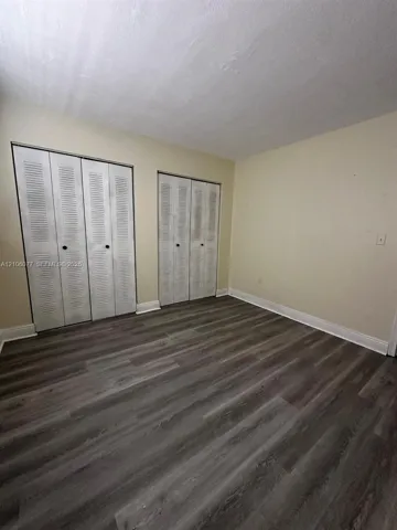 Wood-finish flooring, neutral wall tones, and dual louvered-style bi-fold closet doors