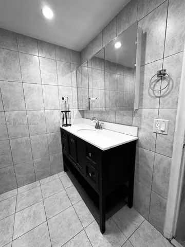 Bathroom vanity featuring a dark-finish wooden base, integrated sink, white countertop, and triple-pane medicine cabinet, complemented by floor-to-ceiling tile wall finishes and ceramic tile flooring