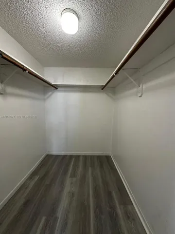 Storage area featuring wood-finish flooring, white walls, integrated shelving, and ceiling-mounted lighting
