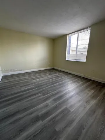 Neutral-toned interior space featuring wood-finish flooring and a single-pane window with horizontal blinds