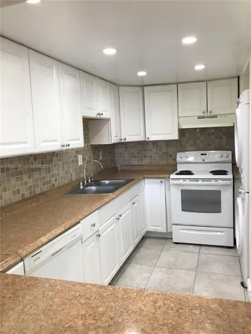 Kitchen featuring white cabinetry, solid-surface countertops, tile backsplash, built-in dishwasher, and recessed lighting