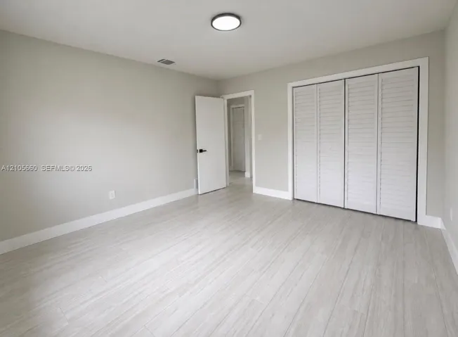 Neutral interior featuring wood-finish flooring, white louvered-style closet doors, and flush-mount ceiling lighting
