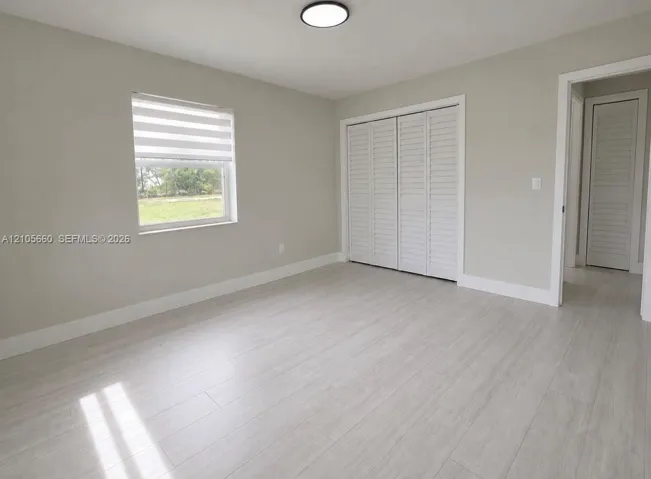 Interior space featuring wood-finish flooring, neutral wall paint, bi-fold closet doors, a flush-mount ceiling light fixture, and a window with a roller shade