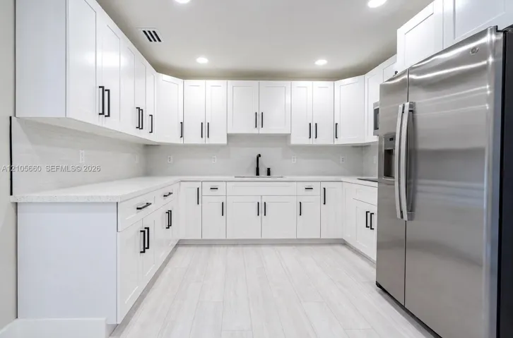 Kitchen featuring white shaker-style cabinetry, solid-surface countertops, horizontal tile backsplash, stainless steel refrigerator, and wood-finish flooring