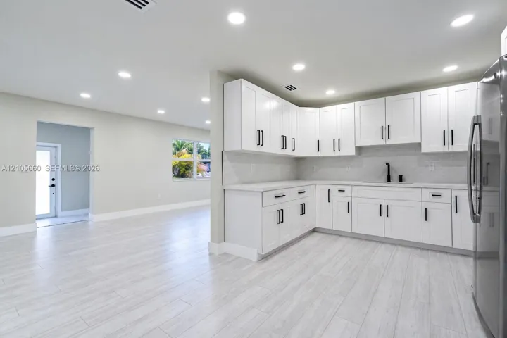 Kitchen featuring white shaker-style cabinetry, solid-surface countertops, subway tile backsplash, recessed lighting, and wood-finish tile flooring