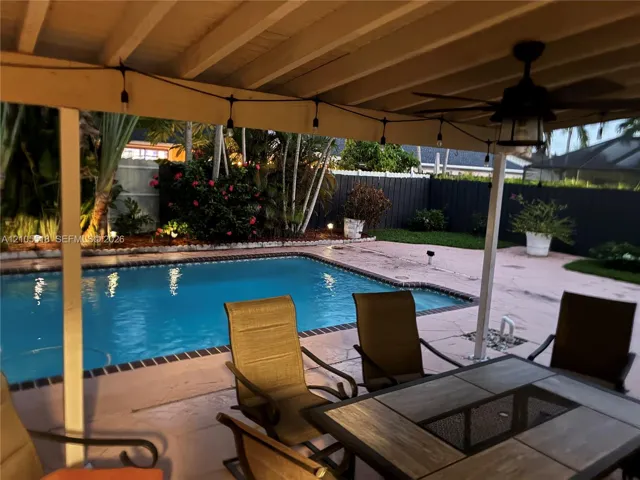 Covered patio featuring a ceiling fan, swimming pool with tiled coping, concrete pool deck, and perimeter privacy fencing