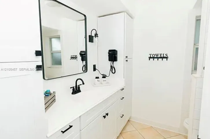 White shaker-style cabinetry with matte black hardware, integrated tall storage, rectangular framed mirror, and dual-handle matte black faucet