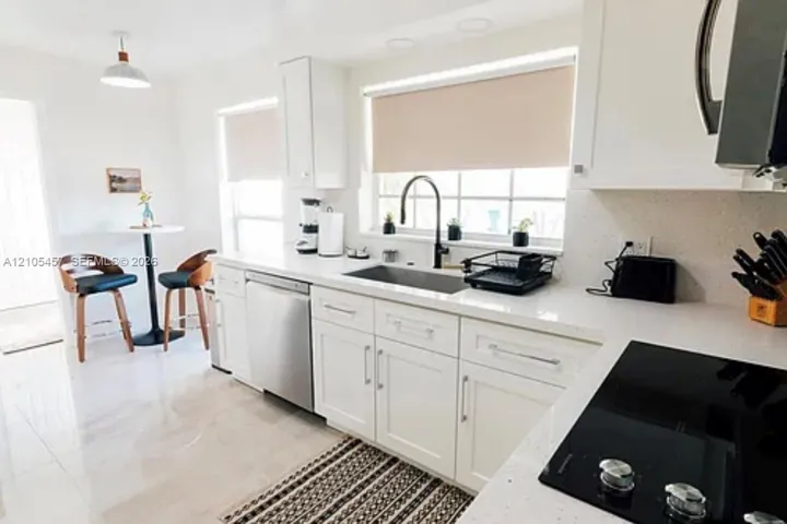 Kitchen featuring white cabinetry, solid-surface countertops, a stainless steel dishwasher, a recessed sink with a matte black faucet, and a black electric cooktop