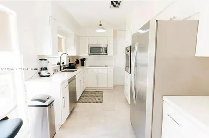 Kitchen featuring white cabinetry, solid-surface countertops, stainless steel appliances, and a recessed sink with a high-arch pull-down faucet