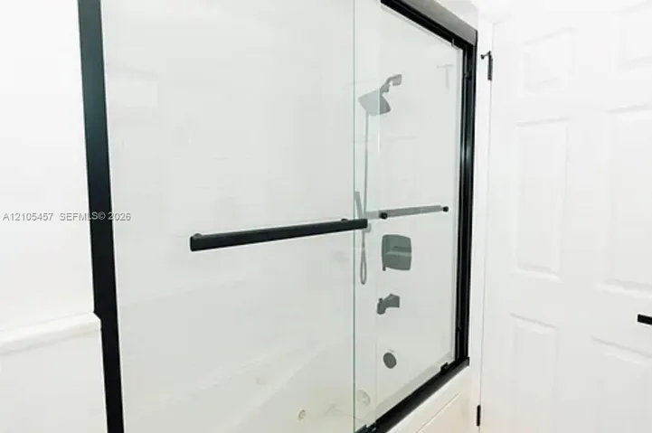 Frameless glass shower enclosure with matte black hardware, integrated handheld showerhead, wall-mounted fixtures, and six-panel interior door