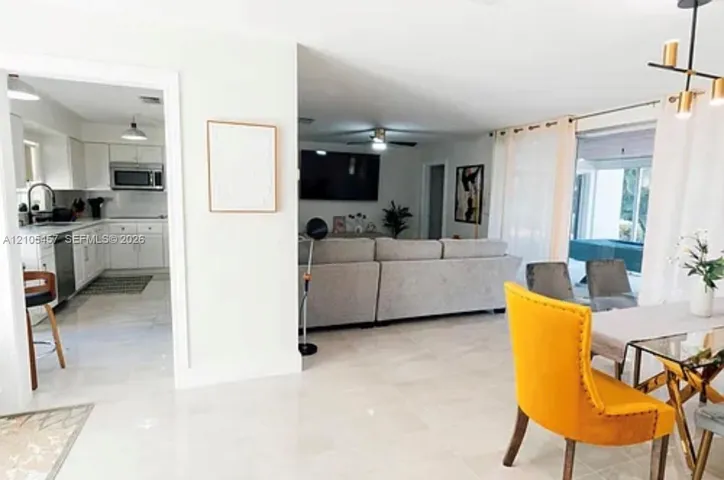 Open-concept floor plan featuring large-format tile flooring, white cabinetry, integrated stainless steel appliances, and a modern multi-light chandelier