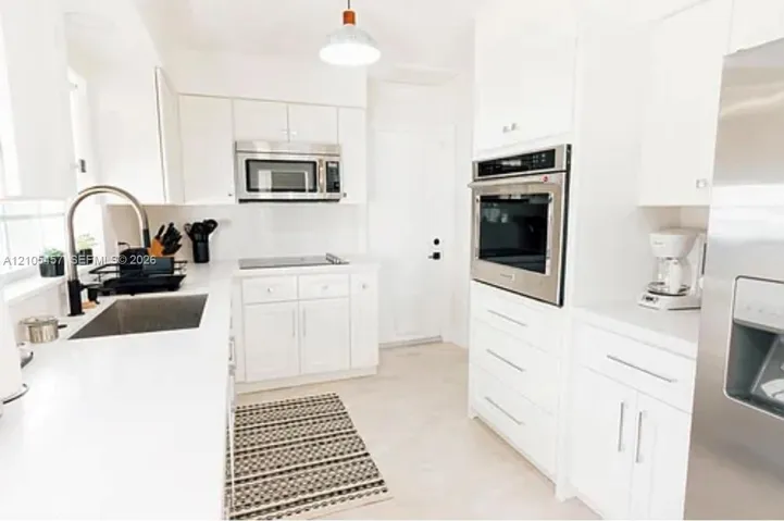 Kitchen featuring white cabinetry, solid surface countertops, stainless steel wall oven, over-the-range microwave, and stainless steel undermount sink with a high-arch faucet