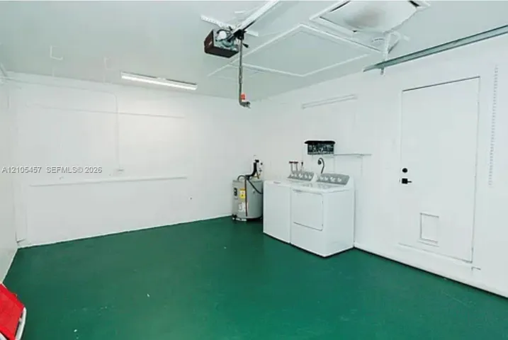 Garage space featuring painted concrete flooring, white walls, overhead lighting, an automated door opener system, and a dedicated laundry area