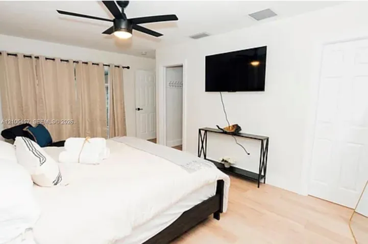 Bedroom featuring light-tone wood-finish flooring, matte black ceiling fan with integrated lighting, and white six-panel interior doors
