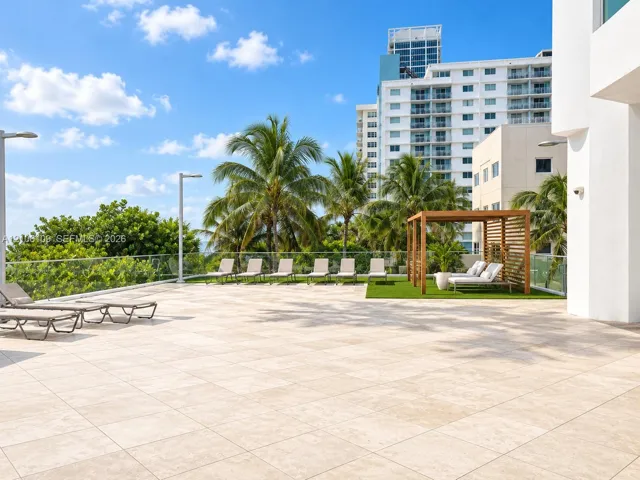 Expansive rooftop terrace featuring large-format stone tiling, glass panel railing, a wood-slat pergola, and synthetic turf area