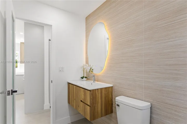 Floating wood-finish vanity with an integrated sink, organic-shaped backlit mirror, and textured tile wall accent