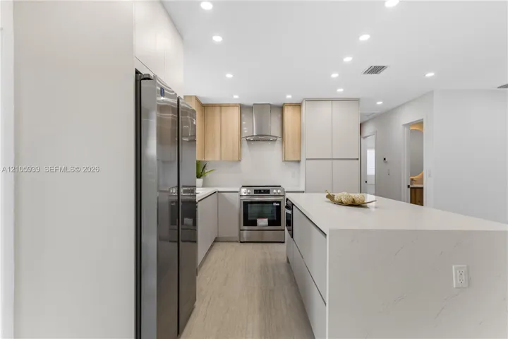 Kitchen featuring a waterfall-edge stone island, stainless steel appliances, a modern stainless steel range hood, dual-tone cabinetry, and wood-finish flooring