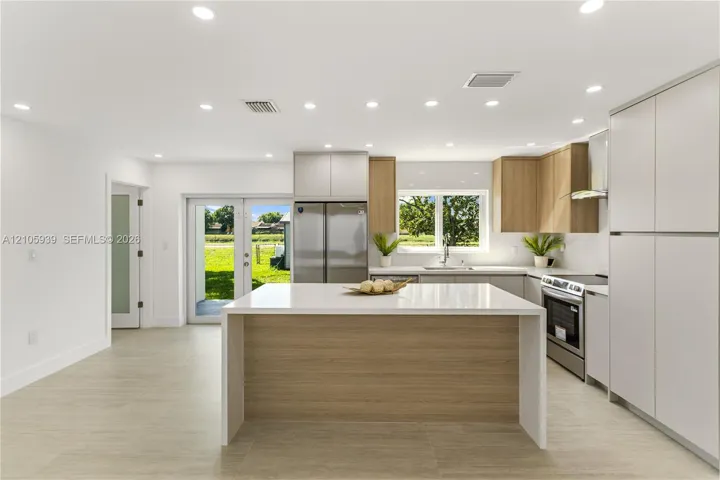 Kitchen featuring two-tone cabinetry, a central island with white stone-finish countertop, stainless steel appliances, recessed ceiling lighting, and wood-finish flooring