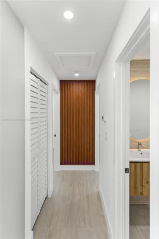 Hallway featuring wood-slat accent wall, white louvered closet doors, recessed lighting, and wood-finish flooring