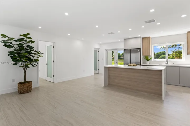 Open concept space featuring light-toned wood-finish flooring, recessed lighting, and a kitchen island with a neutral-toned base
