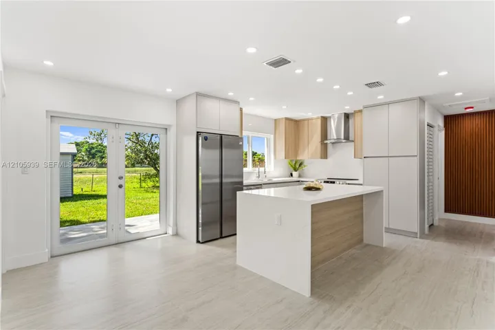 Kitchen featuring a central island with a solid surface countertop, stainless steel refrigerator, recessed lighting, double glass doors, and tile flooring