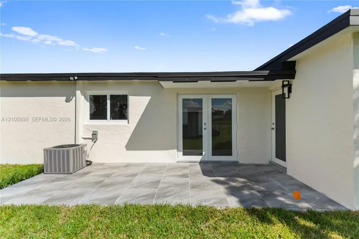 Rear patio featuring large-format gray tile flooring, double-glass entry doors, an attached exterior light fixture, and a stucco finish