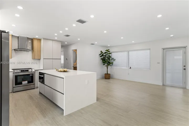 Kitchen featuring a center island with a stone-finish countertop, stainless steel appliances, flat-panel cabinetry, recessed lighting, and wood-finish flooring