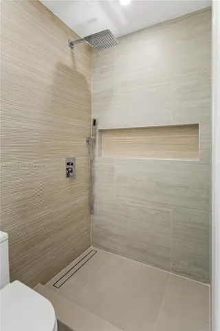 Walk-in shower featuring textured wall tile, large-format smooth wall tile, integrated recessed shelving, square rainfall showerhead with handheld sprayer, and a linear floor drain