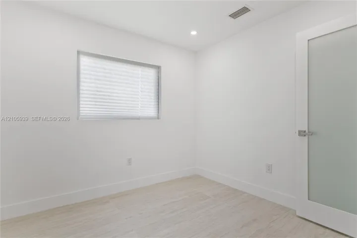 Neutral interior space featuring wood-finish flooring, recessed lighting, and a frosted glass-panel door