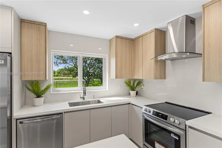 Kitchen featuring light wood-finish cabinetry, stainless steel appliances, solid-surface countertops, a stainless steel undermount sink, and an integrated stainless steel range hood
