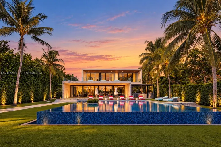 Contemporary two-story residence featuring an expansive infinity-edge pool, tiled patio, glass balcony railing, and manicured landscaping